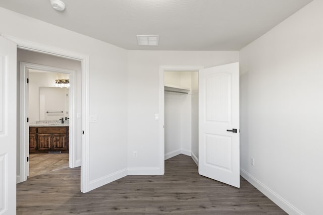 unfurnished bedroom featuring dark hardwood / wood-style floors, ensuite bath, a walk in closet, and a closet