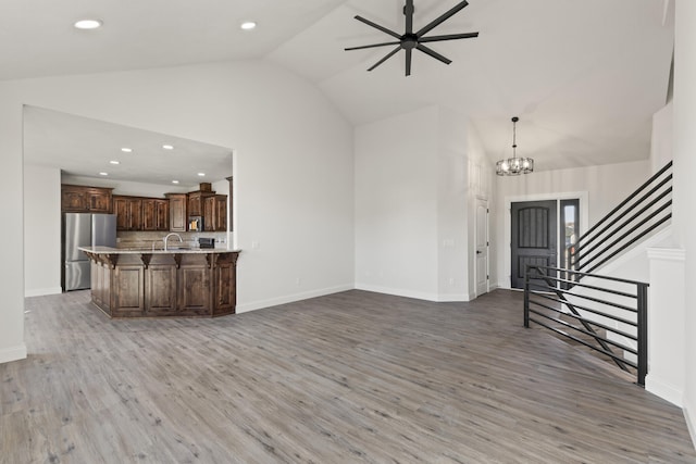 unfurnished living room with ceiling fan with notable chandelier, lofted ceiling, sink, and light hardwood / wood-style flooring