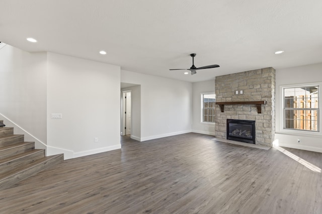 unfurnished living room featuring ceiling fan, a stone fireplace, and dark wood-type flooring