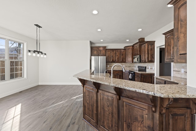 kitchen featuring kitchen peninsula, light hardwood / wood-style flooring, decorative backsplash, dark brown cabinetry, and stainless steel appliances