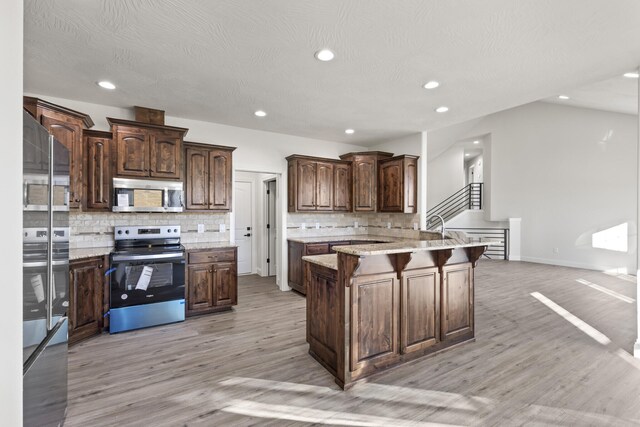 kitchen featuring decorative backsplash, light hardwood / wood-style floors, dark brown cabinetry, and appliances with stainless steel finishes