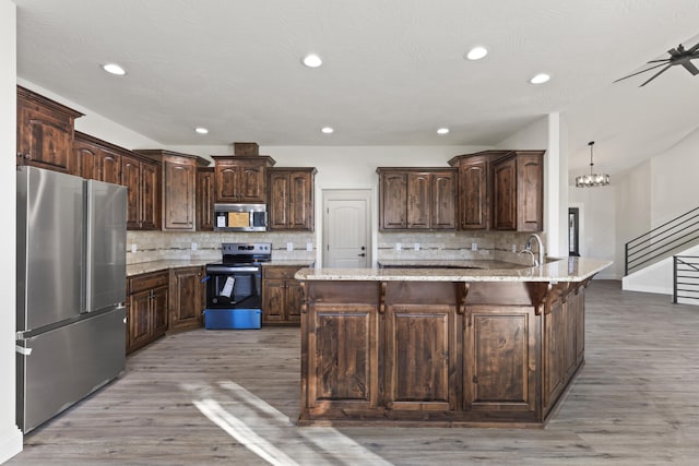 kitchen featuring light stone countertops, kitchen peninsula, decorative backsplash, dark brown cabinets, and appliances with stainless steel finishes