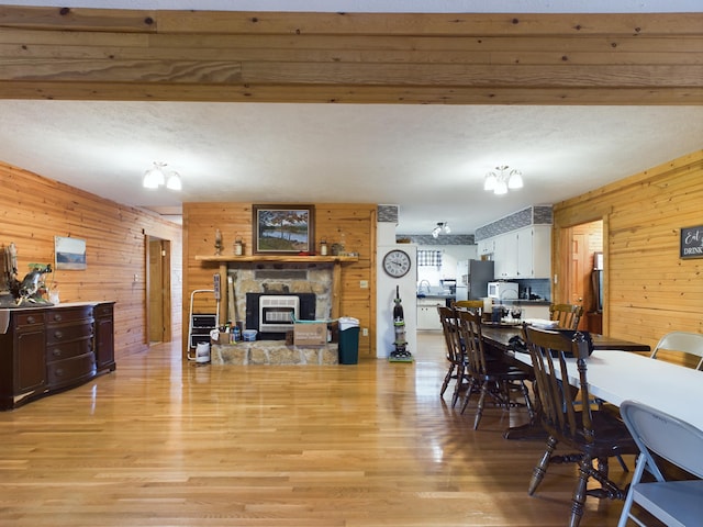 dining room featuring wood walls, a stone fireplace, light wood-type flooring, and a textured ceiling