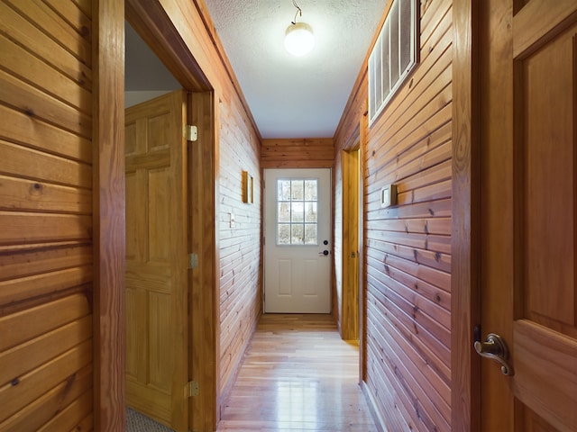 entryway with wooden walls, a textured ceiling, and light wood-type flooring