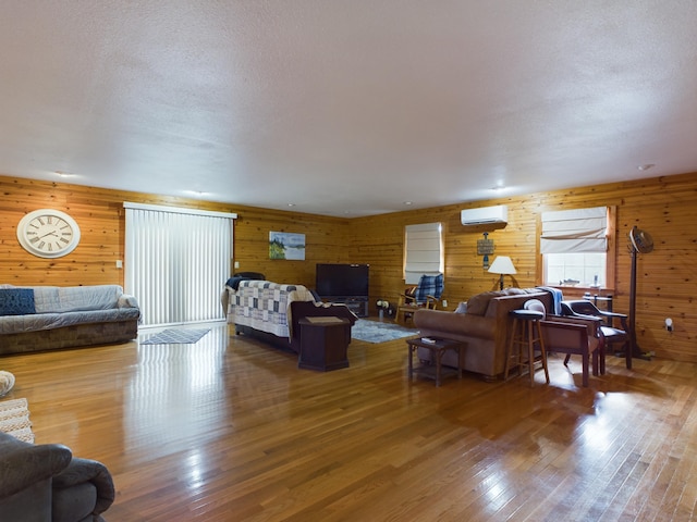 living room with a wall mounted AC, wooden walls, wood-type flooring, and a textured ceiling