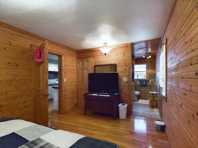 bedroom with wood-type flooring, ensuite bath, and wooden walls