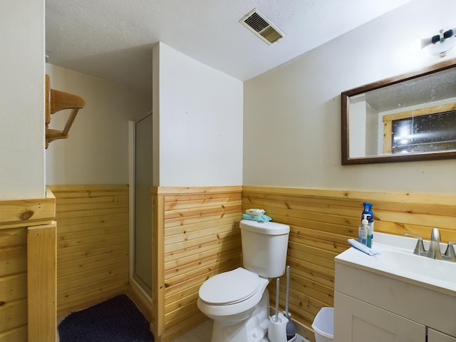 bathroom featuring a textured ceiling, vanity, toilet, and wood walls