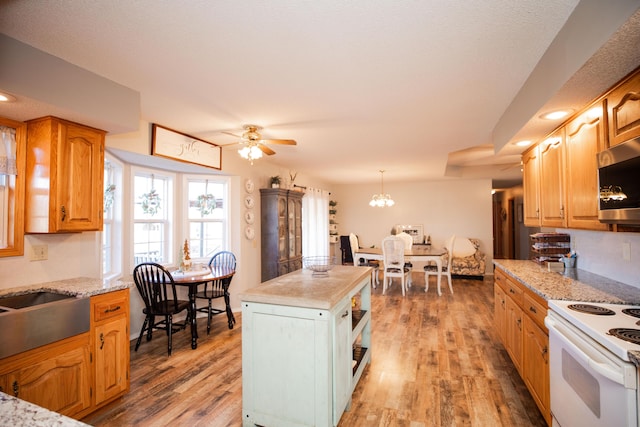 kitchen featuring white range with electric stovetop, decorative light fixtures, ceiling fan with notable chandelier, and hardwood / wood-style flooring