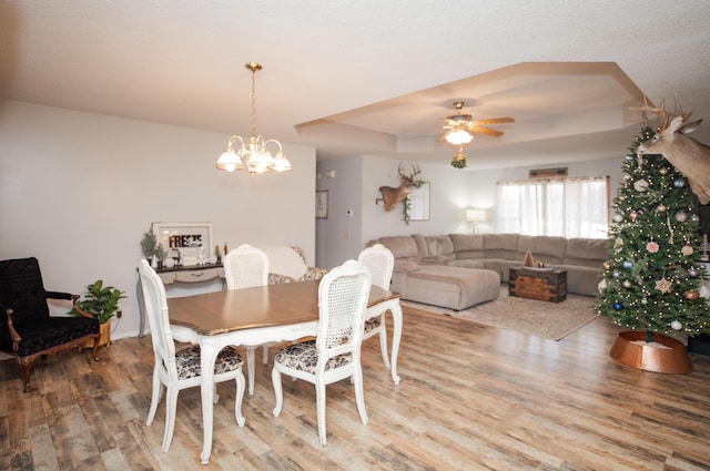 dining area with ceiling fan with notable chandelier, hardwood / wood-style flooring, and a tray ceiling