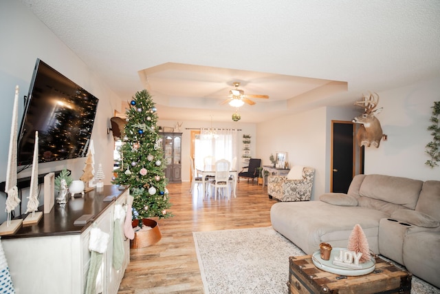 living room featuring a textured ceiling, light hardwood / wood-style floors, a raised ceiling, and ceiling fan