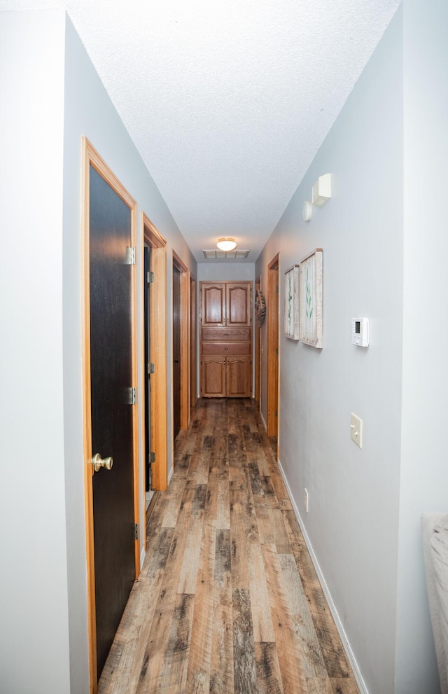 corridor with a textured ceiling and light wood-type flooring