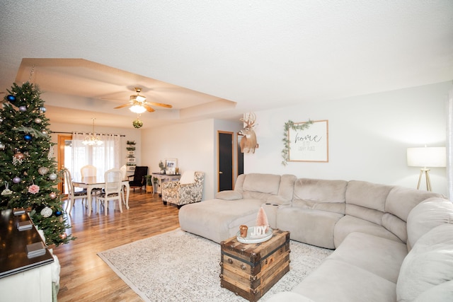 living room featuring ceiling fan with notable chandelier, light wood-type flooring, and a tray ceiling