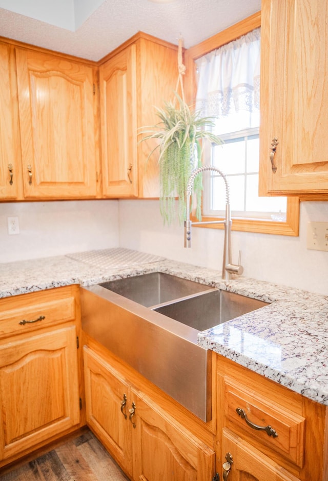 kitchen with a textured ceiling, dark hardwood / wood-style flooring, light stone countertops, and sink