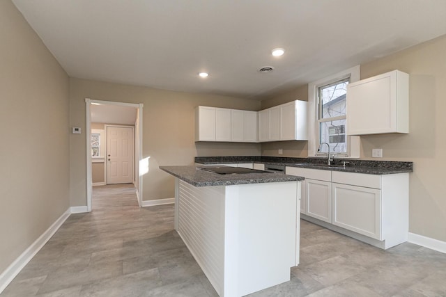 kitchen with white cabinets, black electric cooktop, a kitchen island, and sink