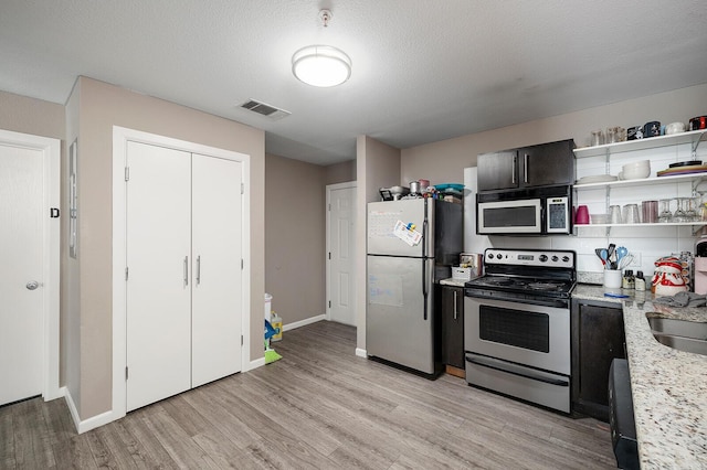 kitchen featuring light stone countertops, a textured ceiling, stainless steel appliances, sink, and light hardwood / wood-style floors