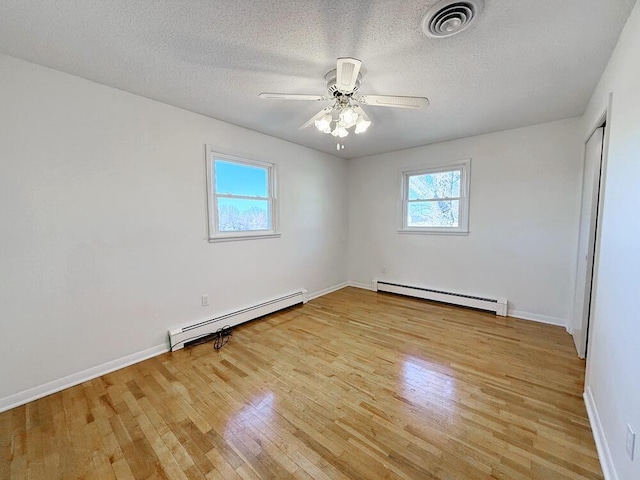 spare room featuring ceiling fan, light wood-type flooring, a textured ceiling, and a baseboard heating unit