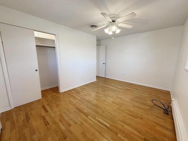 unfurnished bedroom featuring a baseboard heating unit, ceiling fan, a textured ceiling, light hardwood / wood-style floors, and a closet