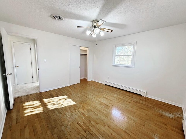 unfurnished bedroom featuring ceiling fan, wood-type flooring, a textured ceiling, and a baseboard heating unit