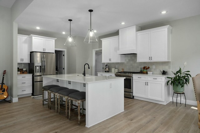 kitchen featuring appliances with stainless steel finishes, a center island with sink, white cabinetry, and pendant lighting