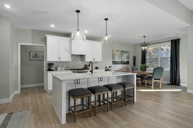 kitchen with white cabinets, an island with sink, decorative light fixtures, and light wood-type flooring