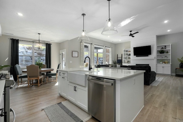 kitchen featuring ceiling fan with notable chandelier, stainless steel appliances, pendant lighting, white cabinets, and an island with sink