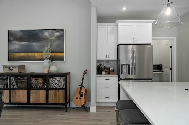 kitchen with stainless steel refrigerator with ice dispenser, tasteful backsplash, hardwood / wood-style flooring, white cabinets, and hanging light fixtures