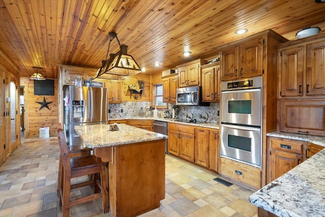 kitchen featuring pendant lighting, a center island, wooden walls, appliances with stainless steel finishes, and light stone counters