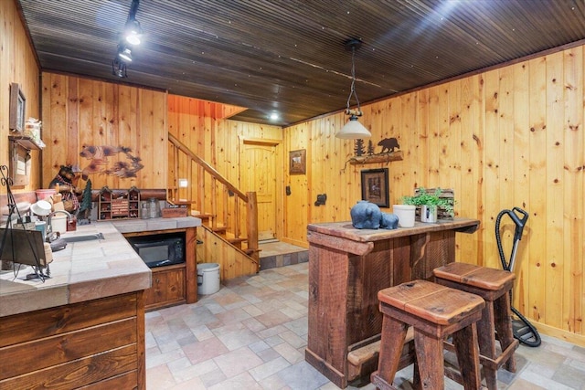 bar with tile countertops, decorative light fixtures, wood walls, and sink