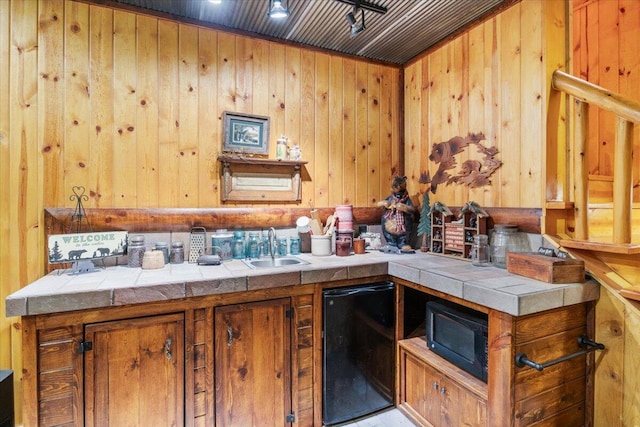 kitchen featuring sink, tile counters, wooden walls, and black appliances