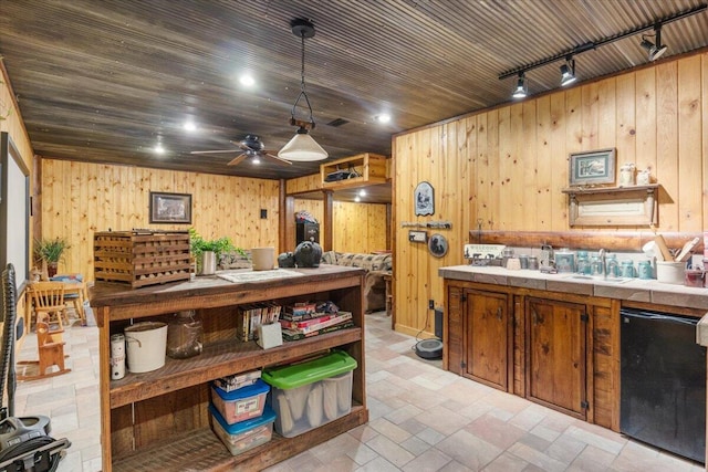 kitchen featuring tile countertops, decorative light fixtures, wood walls, and black dishwasher