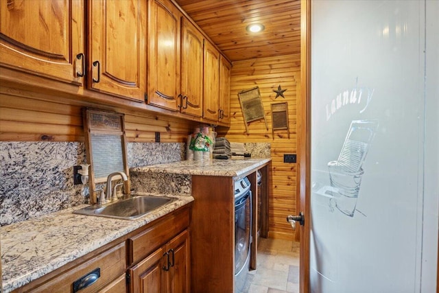 kitchen featuring wooden ceiling, backsplash, sink, wooden walls, and light stone counters