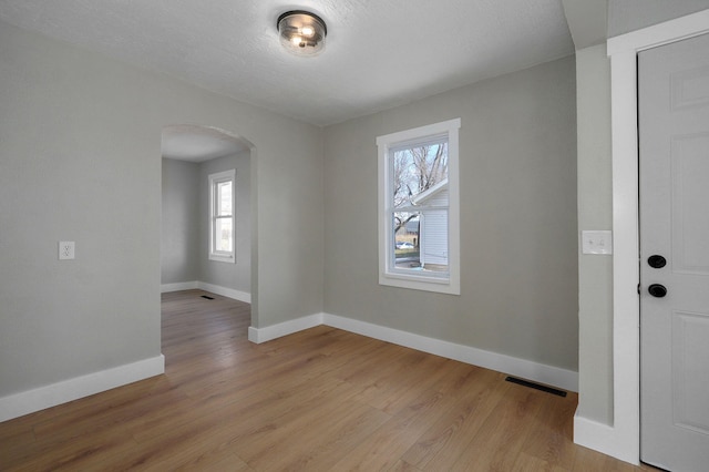 unfurnished room with a textured ceiling, light hardwood / wood-style floors, and a wealth of natural light