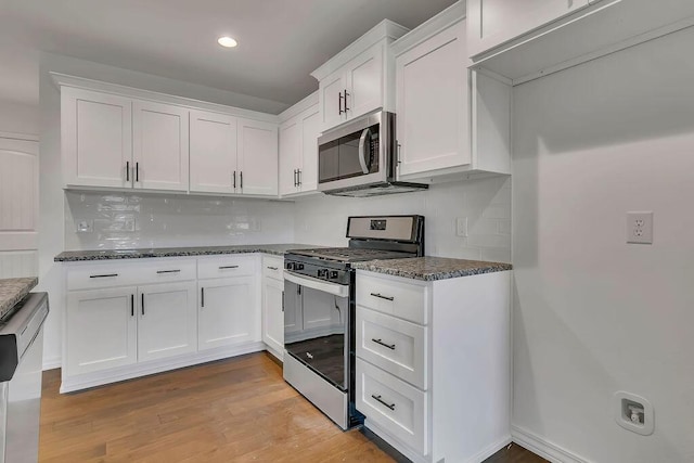 kitchen featuring white cabinetry, dark stone countertops, light wood-style flooring, and appliances with stainless steel finishes