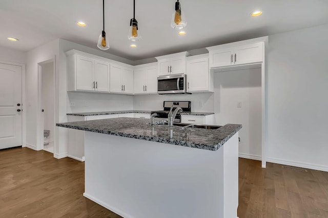 kitchen featuring dark wood-type flooring, dark stone counters, stainless steel appliances, white cabinetry, and a sink