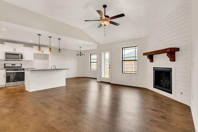 unfurnished living room featuring ceiling fan with notable chandelier, a large fireplace, dark hardwood / wood-style floors, and vaulted ceiling