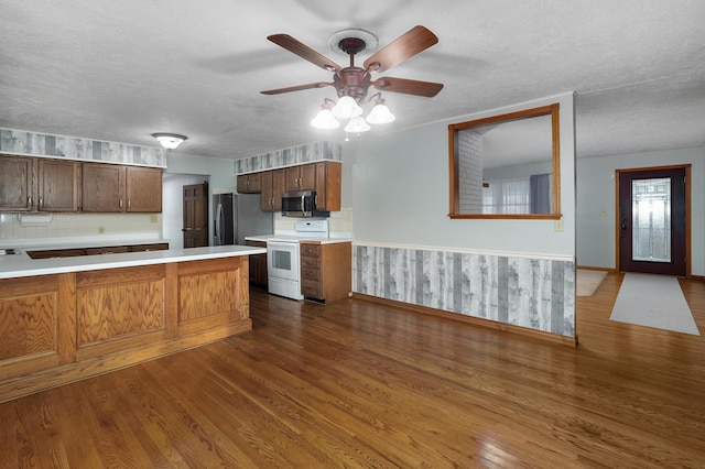 kitchen featuring a textured ceiling, stainless steel appliances, ceiling fan, dark wood-type flooring, and wood walls