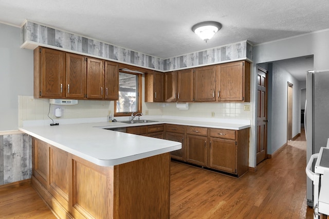 kitchen featuring sink, stainless steel stove, light hardwood / wood-style flooring, a textured ceiling, and kitchen peninsula