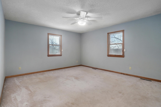 carpeted spare room featuring ceiling fan, a textured ceiling, and a wealth of natural light