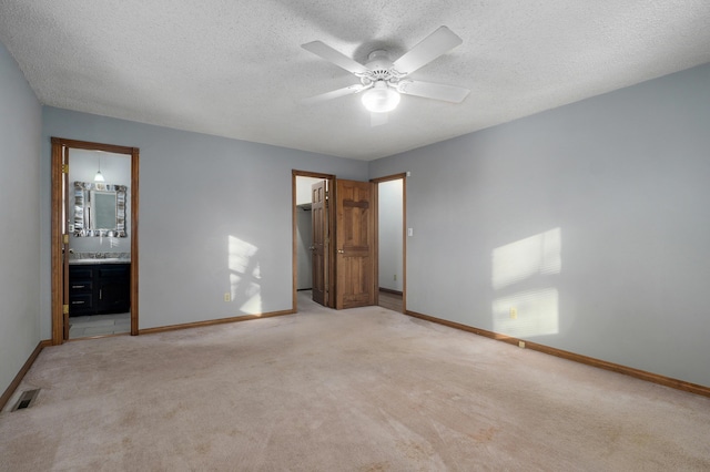 unfurnished bedroom featuring a walk in closet, ensuite bathroom, ceiling fan, and light colored carpet