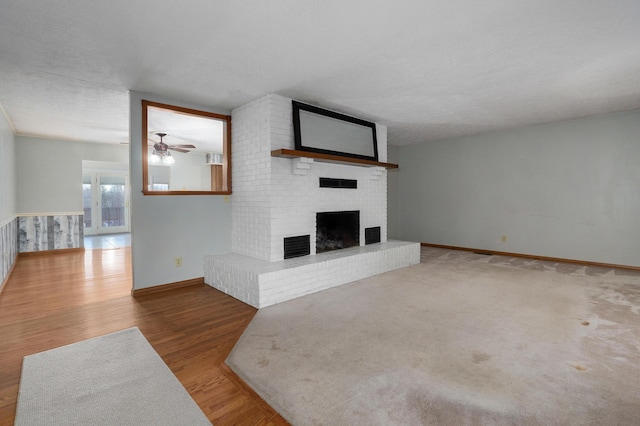 unfurnished living room with ceiling fan, wood-type flooring, a textured ceiling, and a brick fireplace