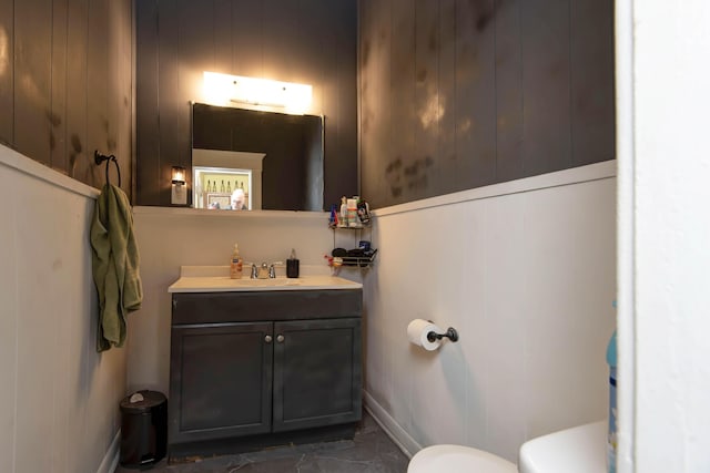 bathroom with vanity, toilet, and wooden walls