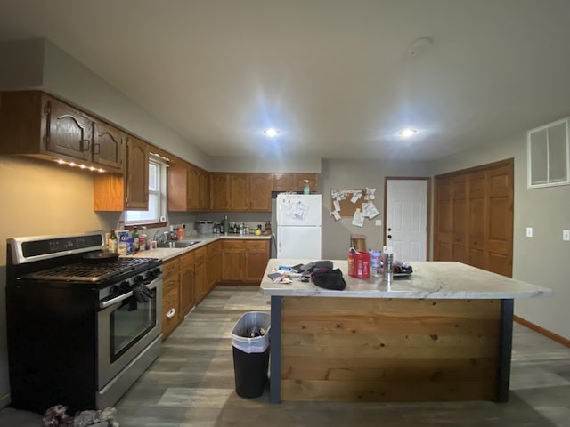 kitchen with gas range, sink, white fridge, a kitchen island, and hardwood / wood-style flooring