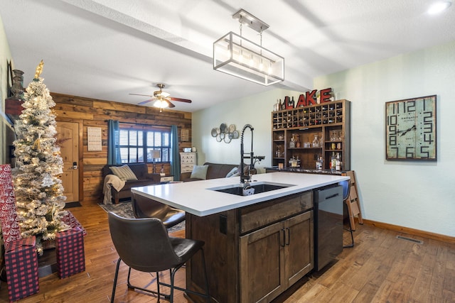 kitchen with dishwasher, an island with sink, dark brown cabinetry, dark hardwood / wood-style flooring, and sink