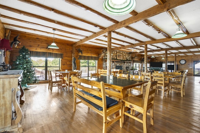 dining space featuring wood walls, beam ceiling, wood-type flooring, and a stone fireplace