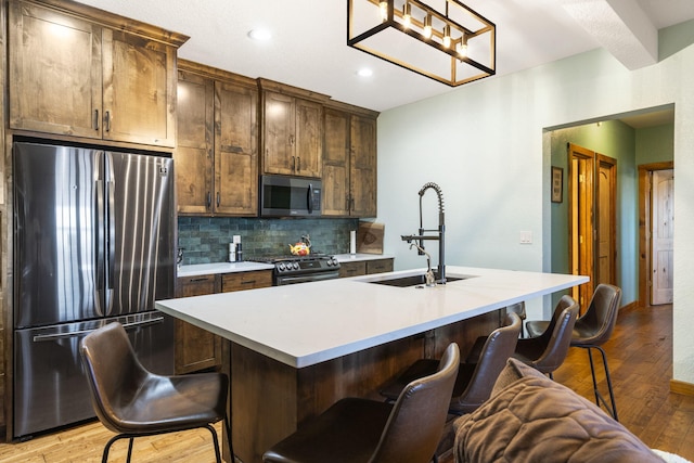 kitchen with appliances with stainless steel finishes, tasteful backsplash, an island with sink, a breakfast bar, and sink