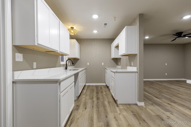 kitchen with light stone counters, ceiling fan, sink, white cabinets, and light hardwood / wood-style floors