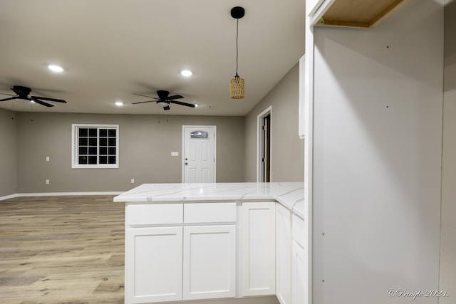 kitchen with white cabinets, hanging light fixtures, light hardwood / wood-style floors, light stone counters, and kitchen peninsula