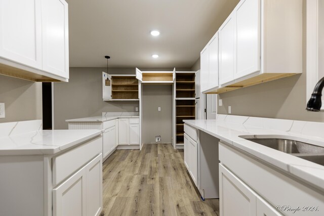 kitchen featuring light stone countertops, light wood-type flooring, sink, decorative light fixtures, and white cabinetry