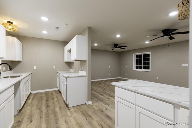 kitchen with white cabinets, sink, ceiling fan, light stone countertops, and light hardwood / wood-style floors