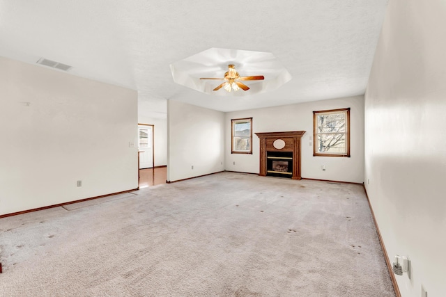 unfurnished living room with a raised ceiling, ceiling fan, light carpet, and a textured ceiling